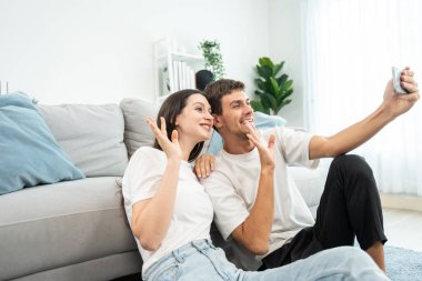 Beyaz tenli çekici çift oturma odasında cep telefonuyla konuşuyor. Çekici erkek ve kadın kendilerini mutlu ve rahat hissediyorlar. Sabahları akıllı telefondan sanal konuşmanın tadını çıkarıyorlar..