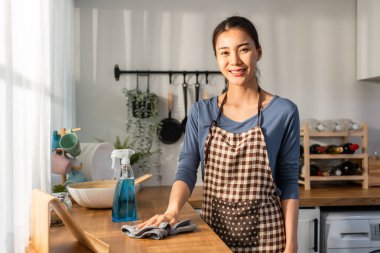 Asyalı güzel temizlikçi kadın evdeki mutfağı temizliyor. Güzel bayan ev hanımı temizlikçi mutlu ve temizlik işleri için kirli yemek masasını siliyor.