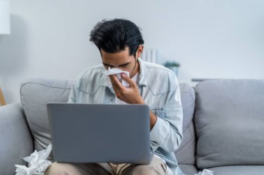 Asyalı yakışıklı erkek, oturma odasında çalışırken burnunu kaçırıyor. Çekici genç adam koltukta oturup kötü hissediyor ve alerji yüzünden acı çekiyor. Sonra da evde hapşırırken burnunu peçete ile örtüyor..