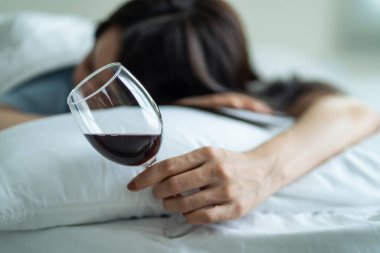 Asyalı genç bunalımlı kadın kalbi kırık ve alkol içiyor. Çekici güzel kız yalnızlık hissediyor, sarhoş ve akşamdan kalma, yatağa uzanmış, oturma odasında bir bardak şarap tutuyor..