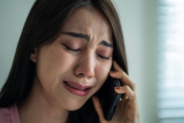 Asyalı üzgün kadın yatakta oturuyor ve cep telefonuyla konuşuyor. Çekici genç kız evde vakit geçirir, sinirli ve hayal kırıklığına uğramış hisseder evde akıllı telefondan konuşur ve iletişim kurar..