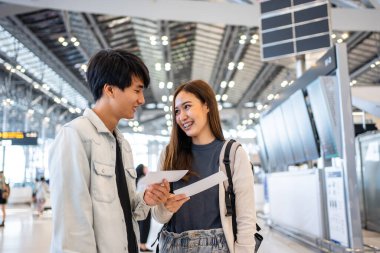 Asyalı genç çift havaalanı terminalinden biniş kapısına doğru yürüyor. Çekici güzel bayan turist arkadaşları tatil gezisi için uçakla yurtdışına gitmekten mutlu ve heyecanlı hissediyorlar..