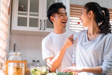 Asyalı genç evli çift evde mutfakta birlikte vakit geçiriyorlar. Çekici erkek ve kadın mutlu ve rahatlar, kahvaltıda yemek pişirmekten mutluluk duyarlar. Aile ilişkisi kavramı.