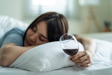 Asyalı genç bunalımlı kadın kalbi kırık ve alkol içiyor. Çekici güzel kız yalnızlık hissediyor, sarhoş ve akşamdan kalma, yatağa uzanmış, oturma odasında bir bardak şarap tutuyor..