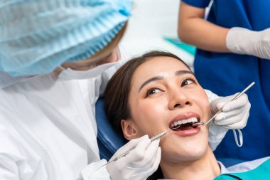 Beyaz dişçi diş sağlığı kliniğindeki genç kız için dişleri muayene ediyor. Diş hekimliği koltuğunda yatan çekici kadın hastanede muayene sırasında doktordan diş tedavisi görüyor.