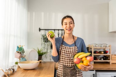 Asyalı genç bir kadının portresi bir kase meyve tutuyor ve kameraya bakıyor. Çekici güzel kız boş zamanlarını evde sağlık hizmetleri için temiz sebzeler yiyerek geçiriyor. Diyet ve Sağlıklı Yemek Konsepti.