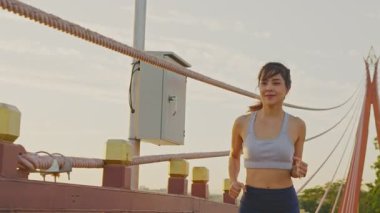 Asyalı genç ve güzel bir kadın gün batımında halk parkındaki köprüde sağlık için koşuyor. Sporcu formda ve sıkı bir kız sağlıklı olması için dışarıda spor yaparak egzersiz yapıyor..