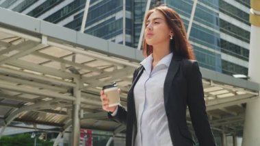 Asyalı genç ve zeki iş kadını şehirde yürüyor. Elinde kahve fincanı tutan kadın çalışma odasına doğru yürüyor.