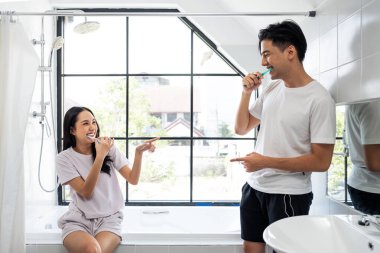 Asyalı yeni evli çift evdeki tuvalette birlikte diş fırçalıyorlar. Çekici genç adam ve kadın mutlu ve rahatlamış hissediyorlar, tatil balayının tadını çıkarıyorlar sonra da birbirlerine evde bakıyorlar..