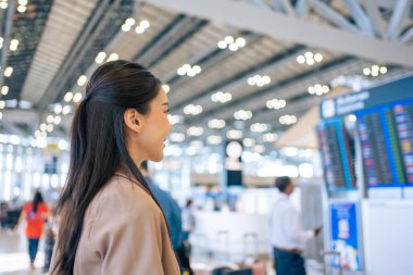 Asyalı genç bir kadın yolcu havaalanından geçiş kartını kontrol ediyor. Çekici güzel bayan turist arkadaşları tatil gezisi için uçakla yurtdışına gitmekten mutlu ve heyecanlı hissediyorlar..