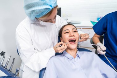 Beyaz dişçi diş sağlığı kliniğindeki genç kız için dişleri muayene ediyor. Diş hekimliği koltuğunda yatan çekici kadın hastanede muayene sırasında doktordan diş tedavisi görüyor.