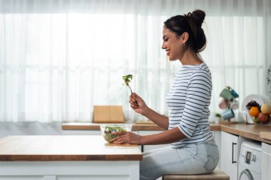 Genç bir kadın evde sağlıklı yeşil salata yiyor. Çekici, güzel vejetaryen kadın kahvaltıda sağlıklı gıdalardan zevk alıyor. Evde kilo vermek ve sağlık hizmeti vermek için..