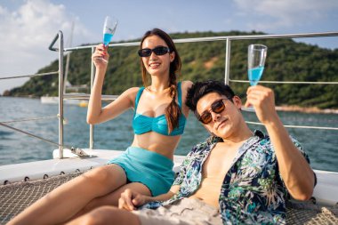 Yatta parti yaparken şampanya içen Asyalı güzel çift. Çekici bir erkek ve kadın birlikte takılıyor, yıl dönümü balayı gezisini kutlarken katamaran teknesi yaz günbatımında yelken açıyor..