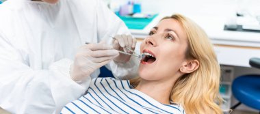 Kadın diş hekimi, diş sağlığı kliniğindeki beyaz dişli kızı muayene ediyor. Diş hekimliği koltuğunda yatan çekici kadın hastanede muayene sırasında doktordan diş tedavisi görüyor.