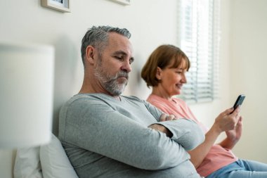 Telefon bağımlılığı, beyaz bir kadın kocasına dikkat etmez. Aile sorunları, yaşlı ve olgun bir çift yatakta oturuyor ve akıllı telefon kullanıyor. Yatak odasında birbirlerini görmezden geliyorlar.