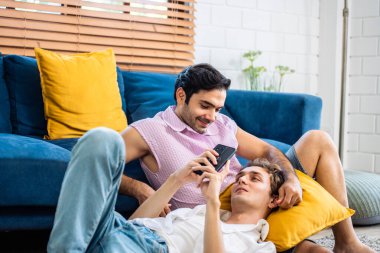 Beyaz, çekici eşcinsel çift oturma odasında telefon saati filmi kullanıyor. Yakışıklı adam LGBTQ ailesi yerde birlikte yatıyor, akıllı telefon konuşmaları yapıyor ve evde online alışveriş yapıyorlar..