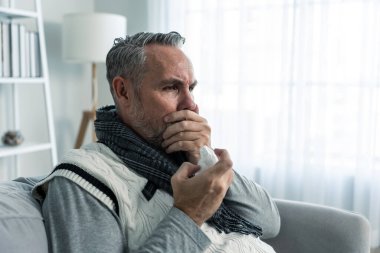 Kafkasyalı kıdemli bir adamın oturma odasında hapşırması. Çekici, yaşlı bir erkek koltukta oturuyor, kötü hissediyor ve alerjisi var. Sonra da evde hapşırırken burnunu peçeteyle kapatıyor..