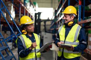 Çeşitli endüstriyel işçi ekipleri fabrikada birlikte çalışıyor. Çekici endüstri mühendisleri miğfer takar ve siparişleri ve ürünleri fabrika deposunda mutlulukla işlerler.