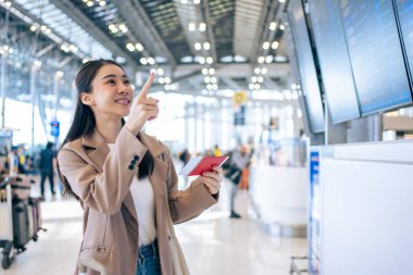 Asyalı genç bir kadın yolcu havaalanından geçiş kartını kontrol ediyor. Çekici güzel bayan turist arkadaşları tatil gezisi için uçakla yurtdışına gitmekten mutlu ve heyecanlı hissediyorlar..