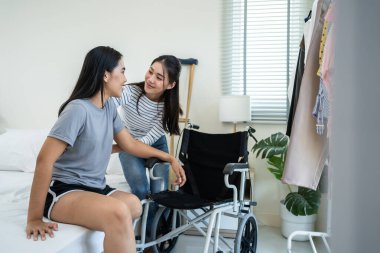 Asyalı bir kadın, tekerlekli sandalyede oturan, bacak kesen bir arkadaşını destekliyor. Çekici, mutlu, bacaksız genç bir kız. Evde, yatak odasında oda arkadaşıyla fizyoterapi yapıyor. Evde boş zaman aktivitesi
