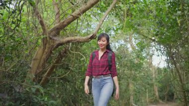 Asyalı genç kadın yeşil orman yolunda yürüyor..