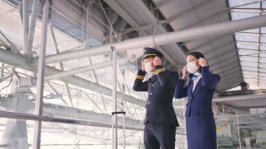 Uçak pilotu ve hostesi Coronavirus enfeksiyonunu önlemek için COVID salgını sırasında havaalanı terminalinde yüz maskesi takıyor..