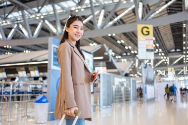 Asyalı genç bir kızın portresi havaalanı terminalinden biniş kapısına doğru yürüyor. Çekici, güzel bayan turist tatil gezisi için uçakla yurtdışına gittiği için mutlu ve heyecanlı hissediyor..