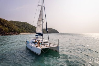 Yaz boyunca okyanustaki lüks özel yatın havadan görünüşü. Çekici genç erkek ve kadınlar birlikte takılıyor, tatil tatilini kutlarken katamaran teknesi yaz günbatımında yelken açıyor..