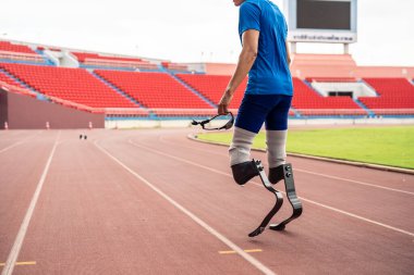 Stadyumda çalışan protez bıçaklı engelli atletlere yakın çekim. Çekici ampüte erkek koşucu egzersizi ve fiziksel sınırlamalardan bağımsız olarak Engelli Olimpiyatları antrenmanı.