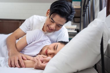 Asyalı yeni evli çift yatağa uzanıp birbirlerine bakıyorlar. Pijamalı çekici genç adam ve kadın evdeki yatak odasında sabahın erken saatlerinde eğleniyorlar. Aile ilişkisi kavramı