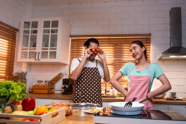 Asyalı genç evli çift evde mutfakta birlikte vakit geçiriyorlar. Çekici erkek ve kadın mutlu ve rahatlar, kahvaltıda yemek pişirmekten mutluluk duyarlar. Aile ilişkisi kavramı.