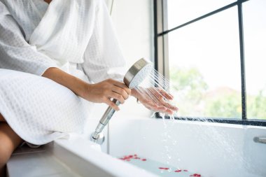 Banyoda duş almak için su hazırlayan bir kadın. Bornozlu çekici kadın köpüğe ve suya dokunuyor ve sabahları sıcacık evdeki spa prosedürlerinin tadını çıkarıyor..