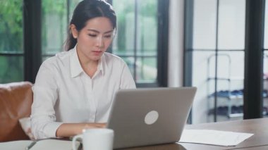 Evde dizüstü bilgisayar ve belgelerle çalışan Asyalı kadın.