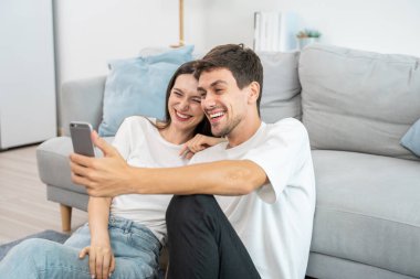 Beyaz tenli çekici çift oturma odasında cep telefonuyla konuşuyor. Çekici erkek ve kadın kendilerini mutlu ve rahat hissediyorlar. Sabahları akıllı telefondan sanal konuşmanın tadını çıkarıyorlar..