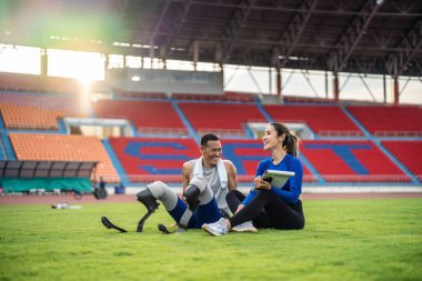 Protez bıçakları ve antrenörü olan Asyalı bir sporcu stadyumda oturuyor. Çekici ampüte erkek koşucu ve genç sporcu Engelliler Koşu Yarışması 'nda antrenman yaptıktan sonra ara veriyor.