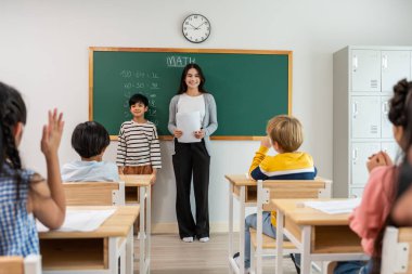 Bir grup öğrenci ilkokulda sınıfta öğretmenle birlikte öğreniyor. Çekici, güzel bayan eğitmen. Anaokulunda küçük çocukları mutluluk ve eğlence ile eğitmek ve eğitmek..