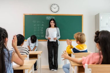 Bir grup öğrenci ilkokulda sınıfta öğretmenle birlikte öğreniyor. Çekici, güzel bayan eğitmen. Anaokulunda küçük çocukları mutluluk ve eğlence ile eğitmek ve eğitmek..