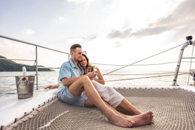 Kafkasyalı romantik çift yat gezisi sırasında güzel manzaraya bakıyor. Çekici bir genç adam ve kadın birlikte takılıp yıl dönümü balayı gezisini kutlarken katamaran teknesi yaz günbatımında yelken açıyor.