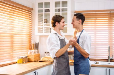 Beyaz, yakışıklı, eşcinsel çift mutfakta şarkı söyleyip dans ediyorlar. Çekici romantik erkek lgbtq çifti önlük giyer, boş zamanlarını geçirir ve evde müzik dinlemekten ve yemek pişirmekten zevk alır..