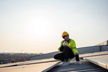 Profesyonel mühendis fotovoltaik panel sisteminin bakımı için çalışıyor. Çatı teftişi yapan çekici teknisyen güneş pili ekipman kutusunu gün batımında güneş pili alanında inceleyip kontrol ediyor.