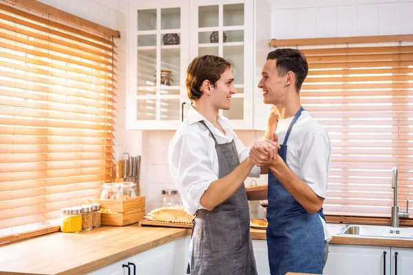 Beyaz, yakışıklı, eşcinsel çift mutfakta şarkı söyleyip dans ediyorlar. Çekici romantik erkek lgbtq çifti önlük giyer, boş zamanlarını geçirir ve evde müzik dinlemekten ve yemek pişirmekten zevk alır..