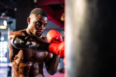 Afrikalı sporcu boksör, koyu renk fitness stadyumunda boks yapıyor. Aktif sporcular boks eldiveni giyer, spor yaparken kum torbasına ya da kum torbasına vurarak spor salonunda sağlığını korumak için spor yapar..