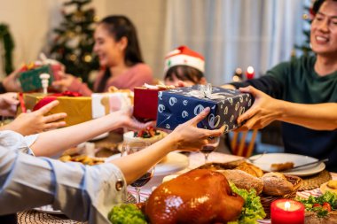 Evde noel partisinde aile hediyelerini değiş tokuş ederken kapatın. Bir grup çekici insan yemek masasında bayram kutlaması yaparken birbirlerinden hediye paketi alıyorlar..
