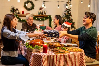 Asyalı sevimli aile evde Noel partisinde hediyelerini değiş tokuş ediyor. Bir grup çekici insan yemek masasında bayram kutlaması yaparken birbirlerinden hediye paketi alıyorlar.