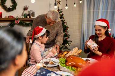 Asyalı aile Noel partisinde küçük kızına hediye paketi veriyor. Çekici küçük kız, yemek yerken akrabalarından hediyeler alır Şükran Günü 'nü birlikte yemek masasında kutlarız.