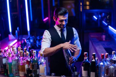 Kafkasyalı barmen bir barda kadınlara kokteyl hazırlıyor. Çekici barmen likör karışımını karıştırıyor. Kokteyl karıştırıcısından, gece kulübü restoranının bardağına..