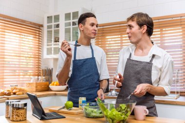 Kafkasyalı genç lgbtq eşcinsel ailesi sabahları evde yemek pişiriyor. Çekici, romantik erkek çift önlük giyer. Mutfakta birlikte kahvaltı yaparken mutlu ve neşeli olurlar.