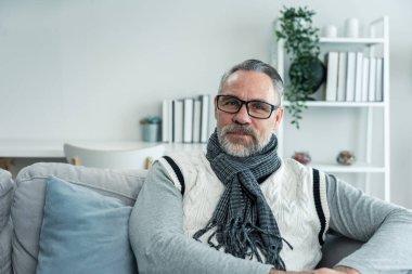 Yaşlı adamın portresi gülümsüyor ve evdeki oturma odasında kameraya bakıyor. Kafkasyalı yaşlı büyükbaba gözlük takar, mutlu olur ve evde emekliliğin tadını çıkarır. Sağlık ve Tıp Konsepti.