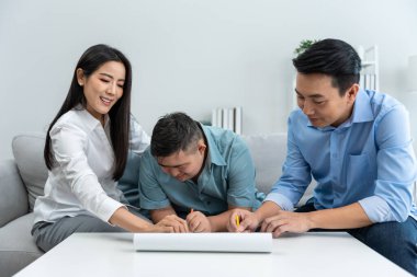 Asyalı mutlu aile, evdeki oturma odasında oğluyla resim çiziyor. Güzel, sevgi dolu anne ve baba evde resim çizmeyi sabırlı bir gence öğretiyor. Yaşam tarzı etkinliği