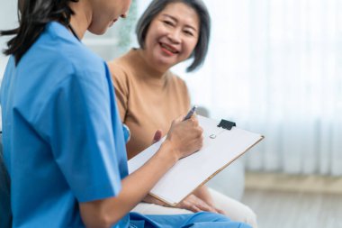 Asyalı genç bakıcı hemşire huzurevindeki yaşlı kadın hastayı muayene ediyor. Çekici uzman bakıcı kadınlar destek oluyor, danışmanlık yapıyor ve evde yaşlı ve mutlu büyükannelere danışmanlık yapıyorlar..